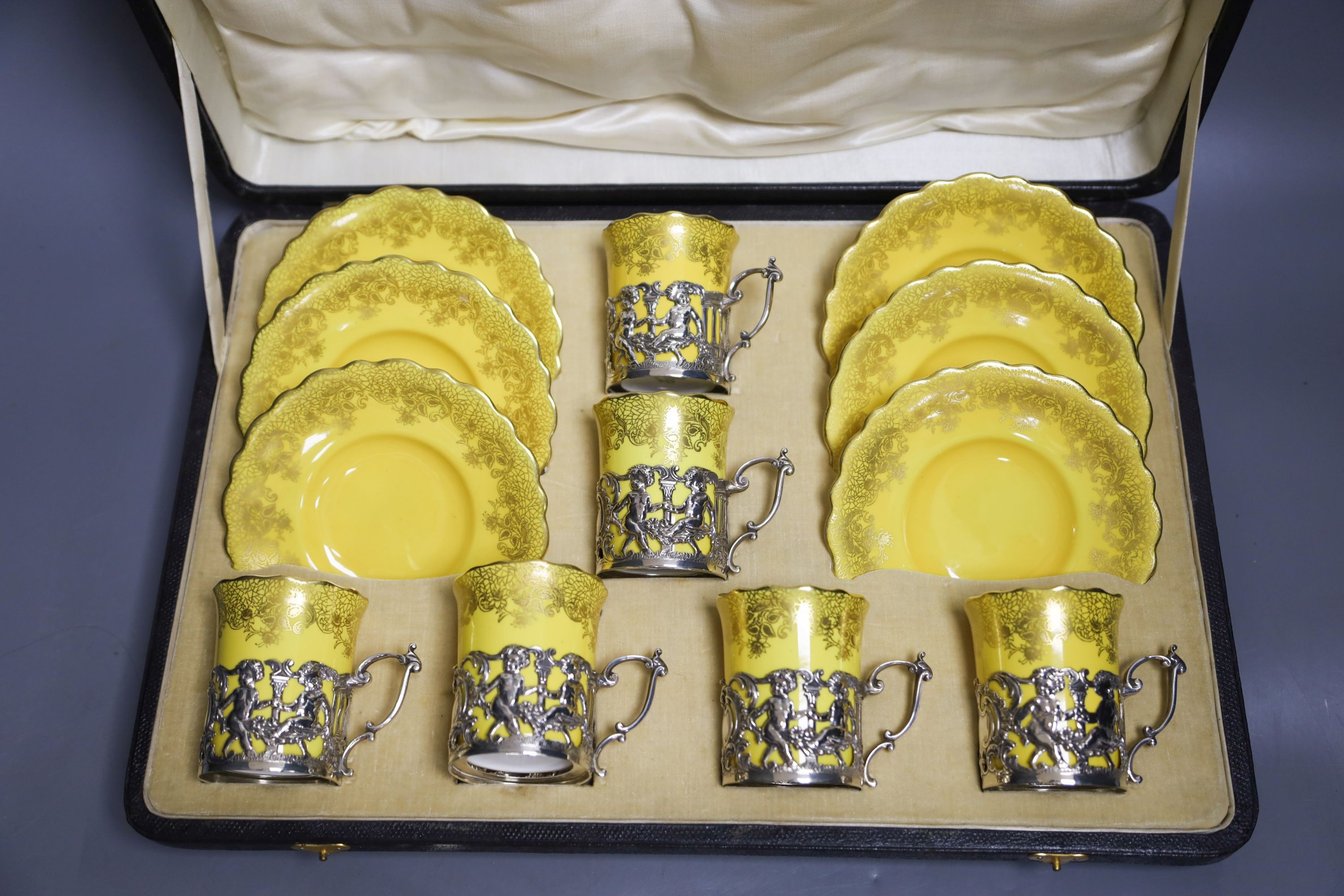 A set of six Aynsley coffee cans and saucers, with silver holders and a set of six silver spoons